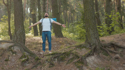 Portrait young man with backpack stand rises hand feel freedom in the forest look around at sunlight nature alone hiking woods activity young vacation attractive autumn hiker travel slow motion