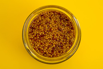 French mustard in a glass jar, shot on a yellow background. Background for seasoning and nutrition.