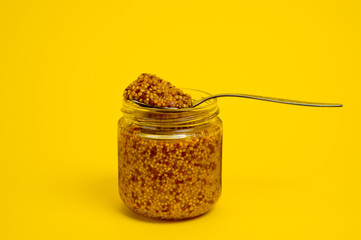 French mustard in a glass jar, shot on a yellow background. Background for seasoning and nutrition.