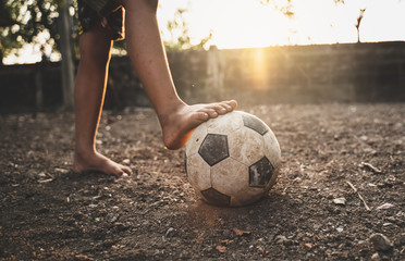 Poor kid playing old soccer or football on ground with glowing sunlight background and hope concept.