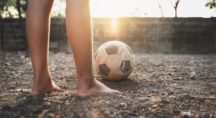 Poor kid playing old soccer or football on ground with glowing sunlight background and hope concept.