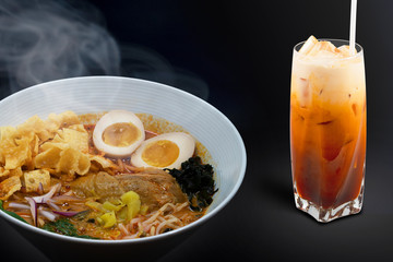 Hot delicious Japanese chicken curry ramen noodles with Orange Thai Ice Tea in black background. Copy Space.