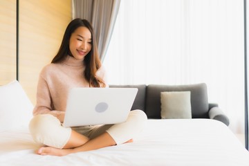 Portrait beautiful young asian woman using laptop with mobile phone on bed
