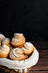 Modern fashionable pastries-cruffins, puff muffin , a mixture of croissants and muffins. On a dark wooden table sprinkled with powdered sugar. Place to copy, view from above