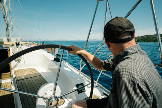 Male skipper on the steering wheel of a yacht. Sailing and yachting concept.