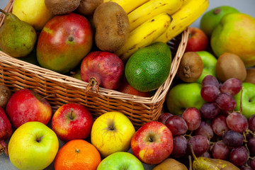 Fruit basket with different fruits. Vitamin set of a healthy diet. Fruit isolated on a gray background. Large set of fruits on a wooden kitchen table. Bananas, apples, pears, pomegranate, tangerine.