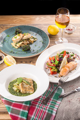 cooked salmon, trout and fish patties with different garnish and glass of white wine on wooden table