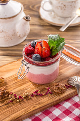 Layered dessert with strawberry and cream cheese panna cotta in glass jar on wooden table