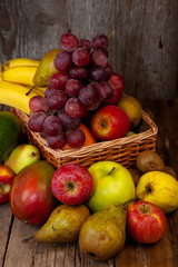 Fruit basket with place for text. Set of different fruits on a wooden kitchen table. Vitamin nutrition, healthy food. Red grapes, blueberries, mangoes, orange, apple, kiwi.