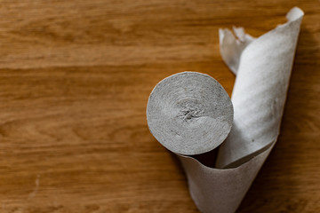 A roll of clean, plain toilet paper, cheap quality, dirty color, lies on a brown wooden table,...