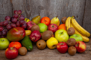 Fruit basket with different fruits. Vitamin set of a healthy diet. Fruit isolated on a gray background. Large set of fruits on a wooden kitchen table. Bananas, apples, pears, pomegranate, tangerine.