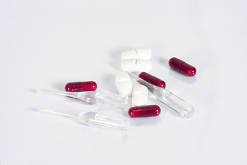 Glass transparent ampoules with liquid, hard tablets, powder medicine capsules, lie on a transparent white table , close-up