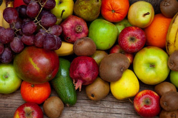 Naklejka na ściany i meble Fruit basket with different fruits. Vitamin set of a healthy diet. Fruit isolated on a gray background. Large set of fruits on a wooden kitchen table. Bananas, apples, pears, pomegranate, tangerine.