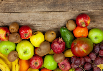 Fruit background with place for text. Different fruits assorted on a wooden table. Vitamin food. Apples, pears, bananas, oranges, kiwi, mango, avocado. A set of healthy food. Frame of fruits. 