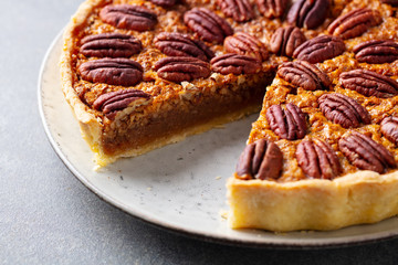 Pecan nut pie, tart on a plate. Grey background. Close up.