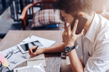 Businessman use mobile phone for talking and right hand use pen for checking data on paper chart, graph.