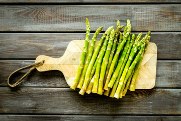 Cooking asparagus. Fresh steams on cutting board on dark wooden background top-down