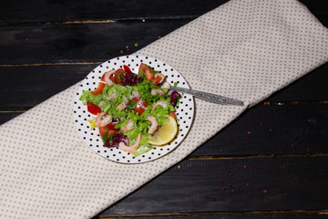 Shrimps and vegetables salad with pepper in polka dot white plate on textile cover on black wooden background