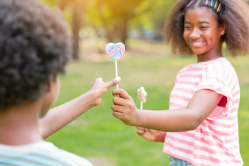 Kids eating lollipop candy together in the park in summer day. Children playing and eating dessert...