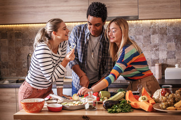 Group of friends preparing vegetarian meal.They preparing food and making fun in the kitchen.