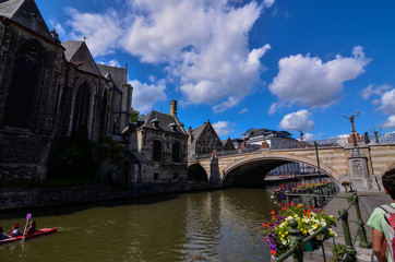 Ghent, Belgium, August 2019. Approaching the historic center, the canal bank with brightly colored planters brings the eye to the St. Michael's bridge. On the left the homonymous church