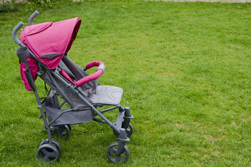 Fototapeta na wymiar baby stroller on the grass,gray and pink color stroller new on grass for baby