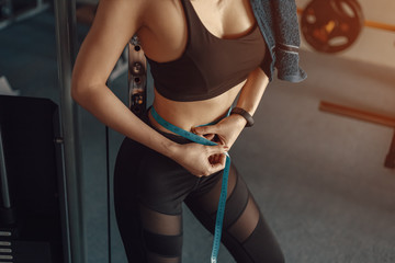 Athletic slim woman measuring her waist by measure tape after workout and exercise in gym.