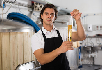 Worried expert is standing with flask for beer and analizying quality