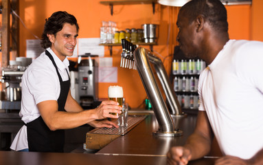 Naklejka na ściany i meble Young man barman giving beer with foam to man client