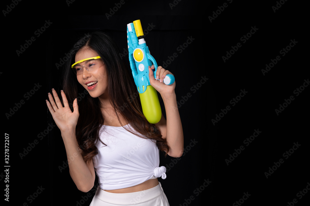 Wall mural Portrait cheerful young asian woman with red glasses holding plastic water gun on balck background. Songkarn festival, Thailand. Thai New Year's Day. Isolated black  background.