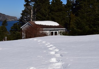 snow shoe tracks in deep snow cabin near the ocean in the background 