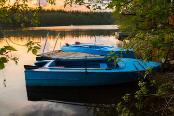 Naklejka na ściany i meble Old fishing boats near wooden jetty. Beautiful russian landscape. Sunset reflection in the water