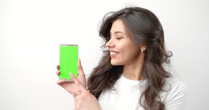 Young pretty brunette woman smiling and touching prekeyed green smartphone screen, technology