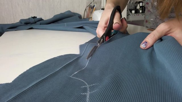 Woman dressmaker cutting fabric textile with scissors