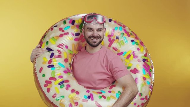 Attractive hipster guy wears swimming glasses posing in donut-shaped inflatable rubber ring enjoying summertime travel. Vacation, swimming season.