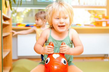 Little girls riding on play horses in kindergarten