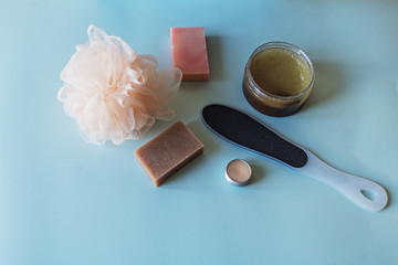 Spa cosmetics, flower soap, handmade sugar scrub with coconut oil in a glass jar, washcloth, face cream and nail file for grinding the skin of the feet on a blue background