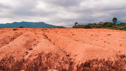 Rough texture of red clay in rural Indonesia with green tropical hills landscape, photographed on a warm day in the hills in Padang, West Sumatra.