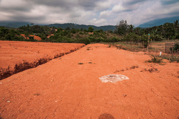 Stretch of red clay flat in rural Indonesia with tropical hills landscape, photographed on a warm day in the hills in Padang, West Sumatra.