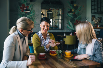 woman showing engagement ring to her friends while drinking coffee in cafeteria