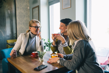 mid aged woman friends talking and drinking coffee in cafe