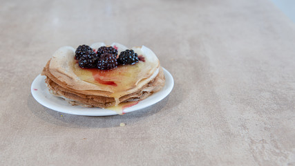 Stack of thin pancakes poured with honey and decorated with fresh blueberries side view with selective focus and light background with copy space