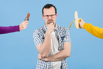 A man faces a choice of something to eat - a banana or a chocolate bar. Bad and healthy snacks