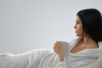 Brunette in bathrobe drinking morning coffee.