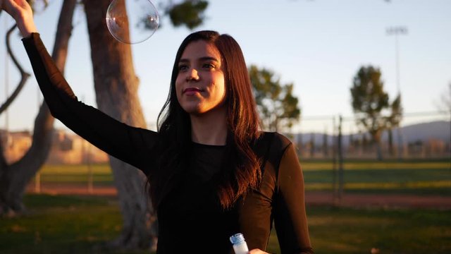 Lovely hispanic woman blowing dreamy bubbles while smiling and laughing with happiness as it pops SLOW MOTION.