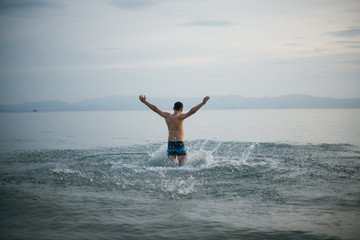 A man enjoys the evening and the ocean at sunset. Young guy in swimming trunks in calm water in the ocean on a tropical island. Holidays in the tropics