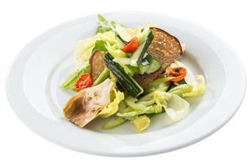 Salad with artichokes, cherry tomatoes, lettuce and rye bread on white plate isolated on white background