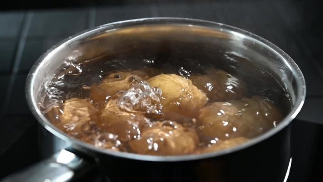 Stainless steel pot of boiling baby potatoes in their jackets or skins in close up high angle with steam rising from the bubbling water