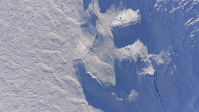 top view aerial over glacier covered in snow wirh clefts and rifts. Winterland outdoor establisher.4k drone overhead forward flight establishing shot. Shadows over snow in sunny day