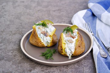 Whole baked potatoes with sour cream, herring and pickled cucumbers sauce on a brown plate on a...